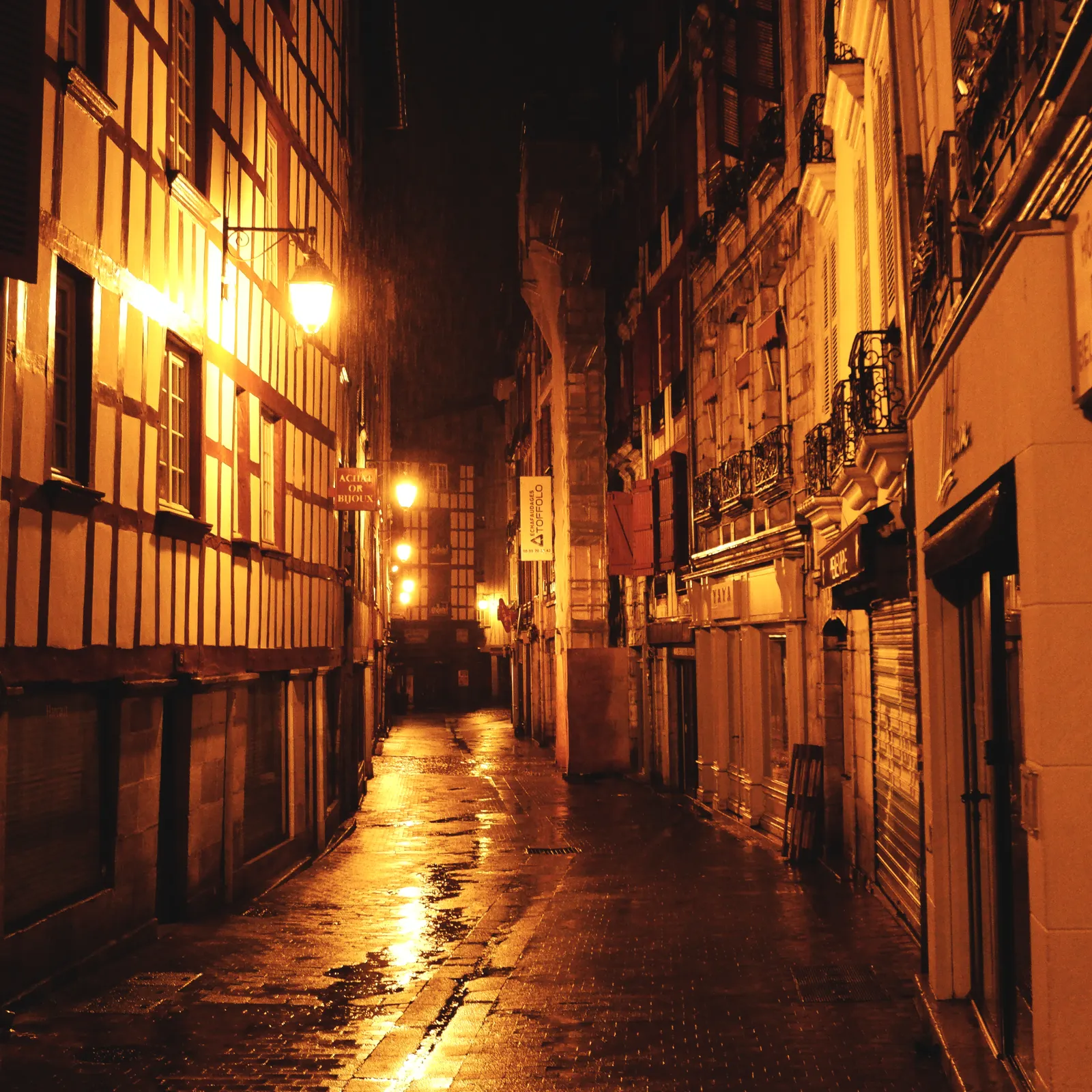 A rain-soaked historic street glowing under lamplight at night